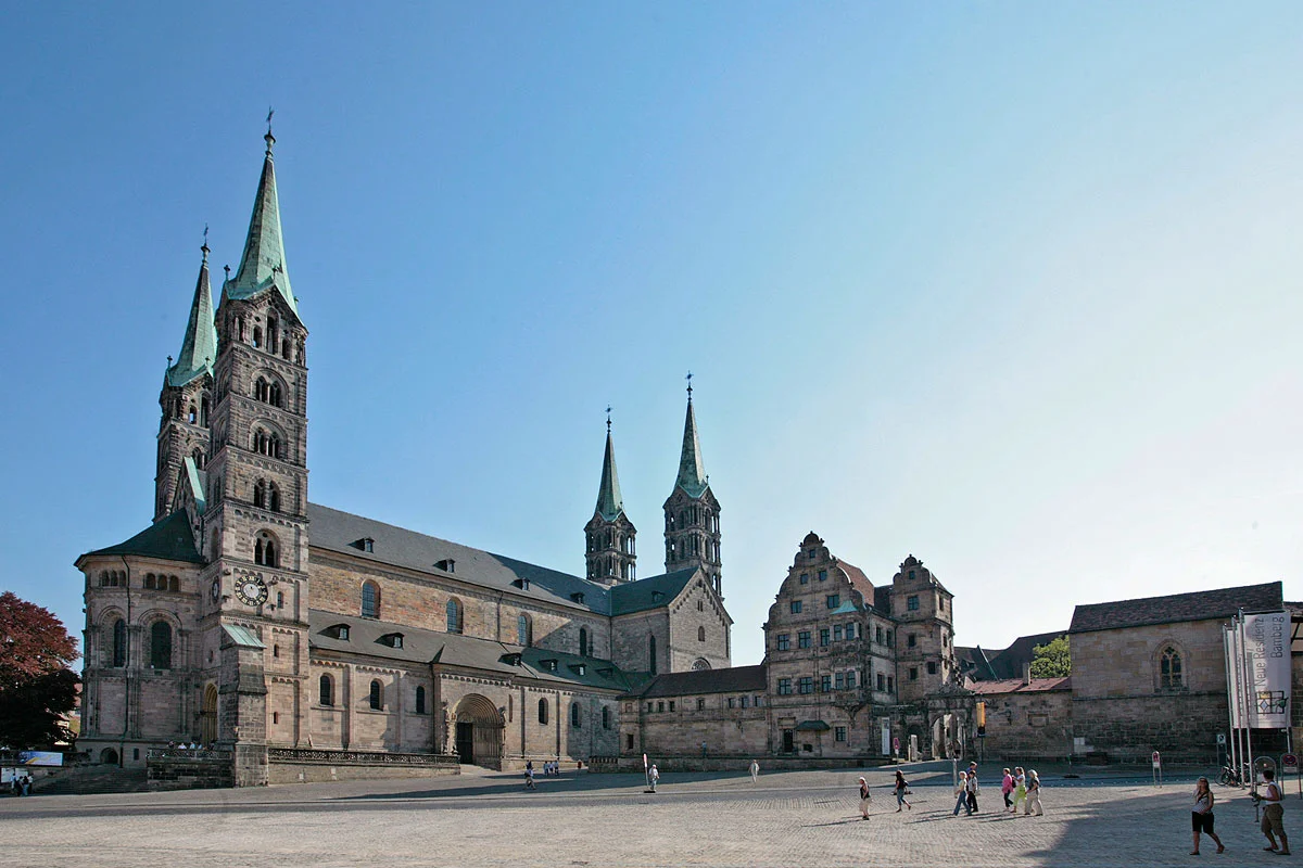 Dom, Alte Hofhaltung und Domplatz Der viertürmige Kaiserdom auf einem der sieben Hügel Bambergs ist das Herzstück der Stadt und das bedeutendste Kunstwerk im weiten Umkreis. Der Kaiserdom St. Peter und Georg geht auf eine Stiftung von Kaiser Heinrich II. zurück, der 1007 das Bistum Bamberg gründete. Zu den größten Sehenswürdigkeiten zählen das Papstgrab von Clemens II., die einzige vom Vatikan anerkannte Grablege eines Papstes nördlich der Alpen, und der Bamberger Reiter. Trotz zahlreicher Nachforschungen ist seine Identität bis heute nicht geklärt, noch viel weniger die des Künstlers.
Die Alte Hofhaltung, deren Kern die einstige Kaiser- und Bischofspfalz bildet, war früher direkt mit dem Dom verbunden. Durch die "Schöne Pforte" gelangt man in den von Fachwerkbauten umgebenen, romantischen Innenhof. Gleich gegenüber befindet sich der Rosengarten.